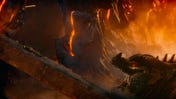 A paladin jumps off a collapsing bridge and towards the open maw of a black dragon below him. Magma, smoke and ash billow around both figures.